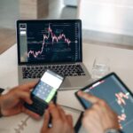 Hands using digital devices for financial analysis at a modern desk setup.