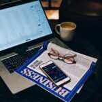 A professional workspace featuring a laptop, smartphone, coffee cup, and business magazine on a table.