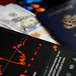 Close-up of smartphone with stock chart, cash, and US passport, symbolizing travel and finance.