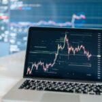 Laptop displaying cryptocurrency trading chart on a white desk.